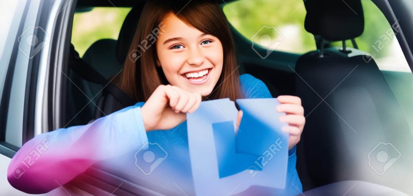 Chica adolescente sonriente sentado en su coche rasgando un signo de l
