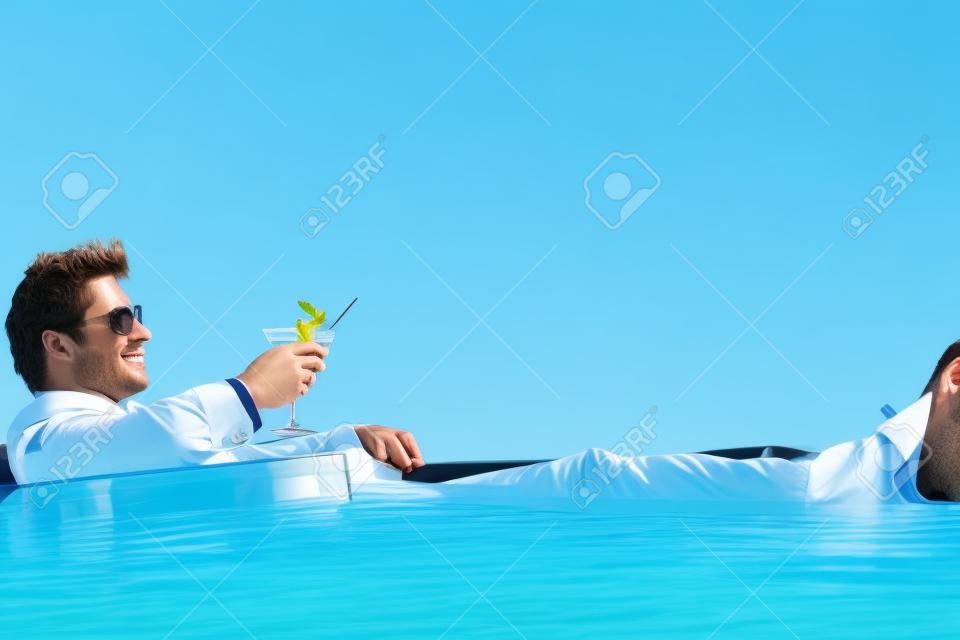 Junger Geschäftsmann Entspannung in einem Pool mit einem Cocktail in einem Anzug