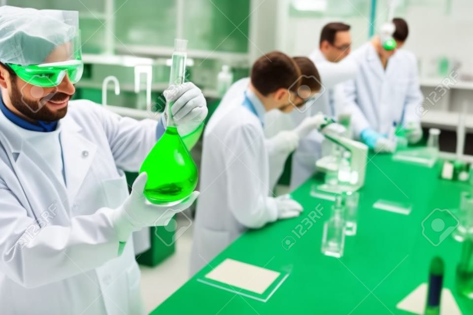 Bir laboratuvarda çalışan ve yeşil bir sıvı inceleyen Kimyacılar