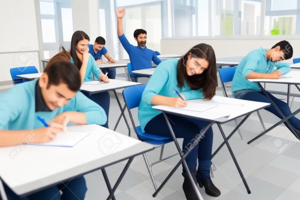 Los estudiantes que se sientan en el salón de clases mientras el estudiante está levantando la mano para hacer la pregunta
