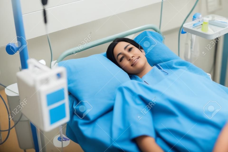 Paciente de sexo femenino acostado en una cama mientras mira a la cámara en la sala del hospital
