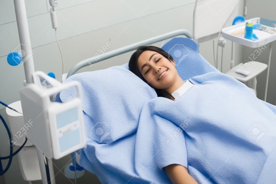 Paciente de sexo femenino acostado en una cama mientras mira a la cámara en la sala del hospital
