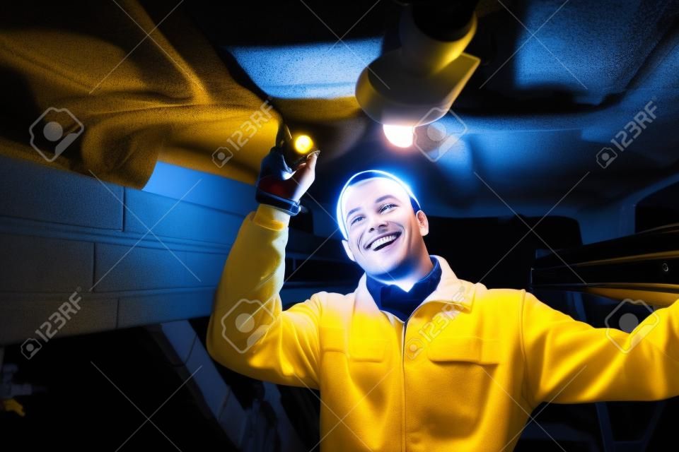 Sourire mécanicien éclairer une voiture avec une lampe de poche dans un garage
