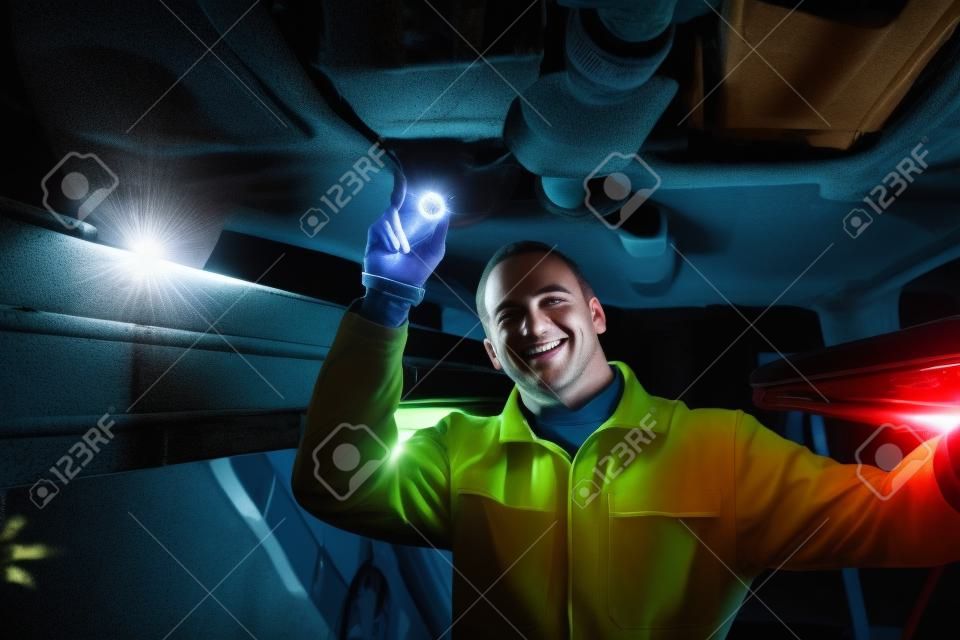 Sourire mécanicien éclairer une voiture avec une lampe de poche dans un garage