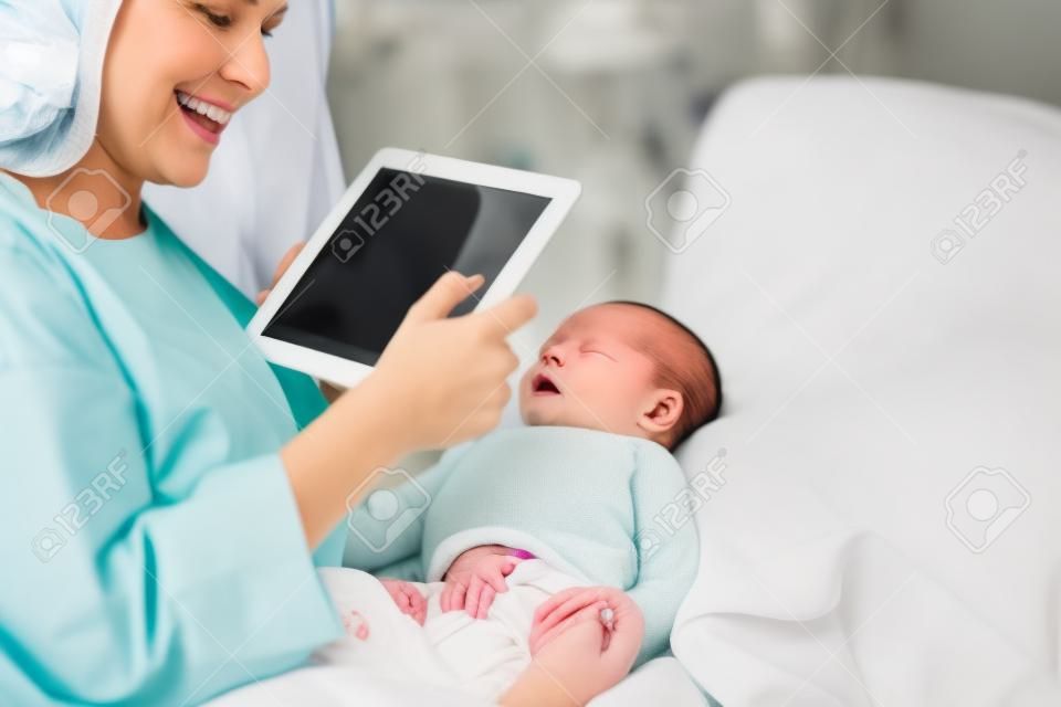 Mother using a tablet to take a picture of a newborn baby in a hospital room
