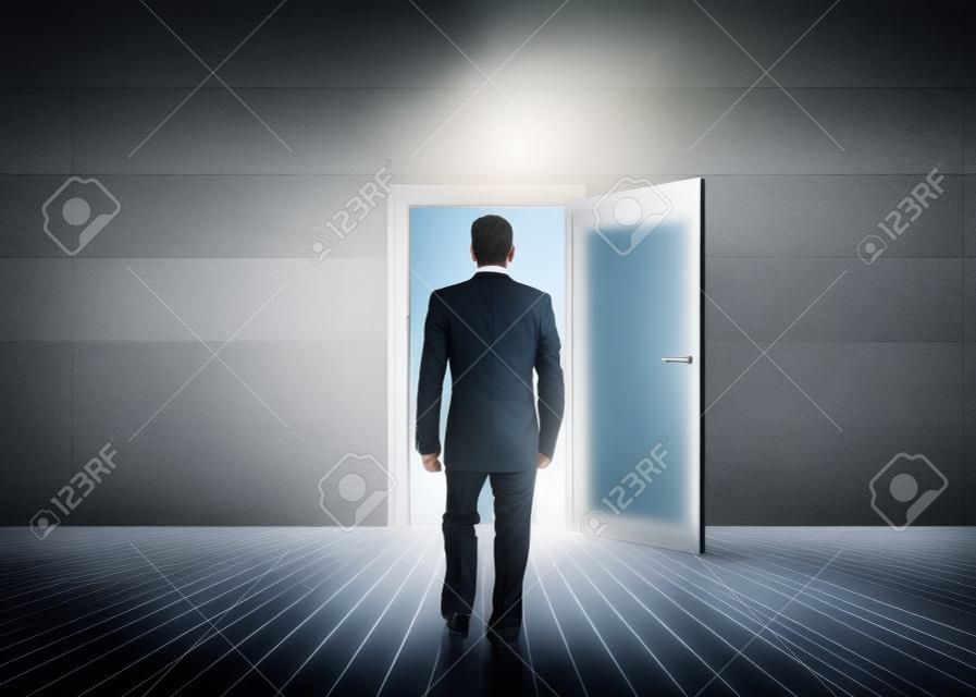 Empresario caminando hacia la puerta que muestra la luz en una habitación gris opaco