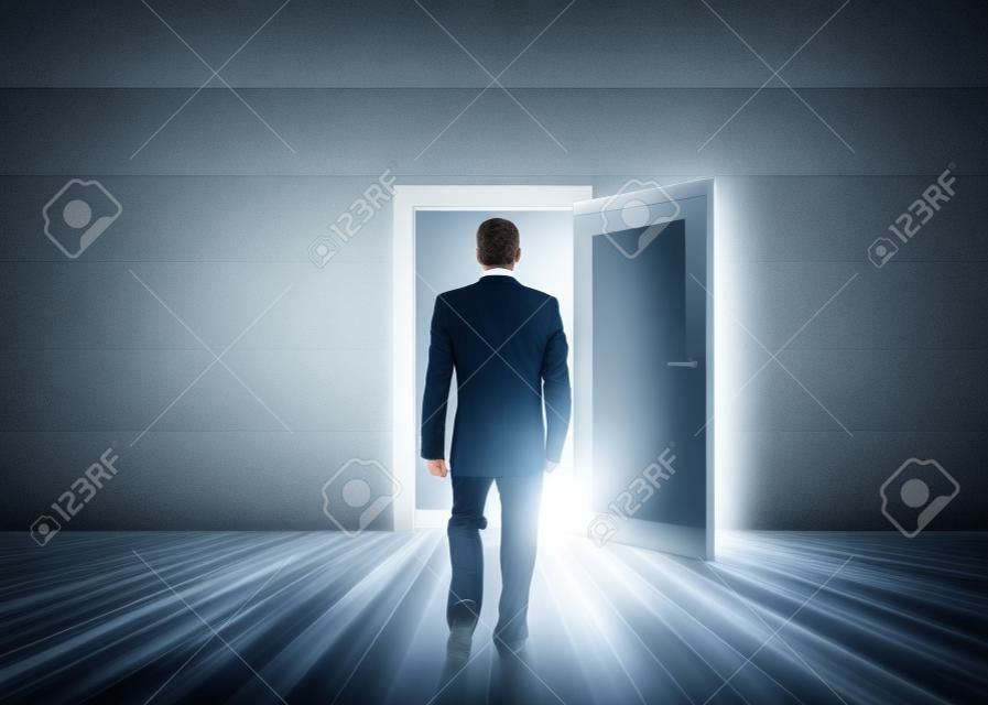 Empresario caminando hacia la puerta que muestra la luz en una habitación gris opaco