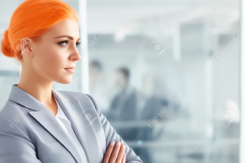 Serious businesswoman standing with arms crossed in a bright office