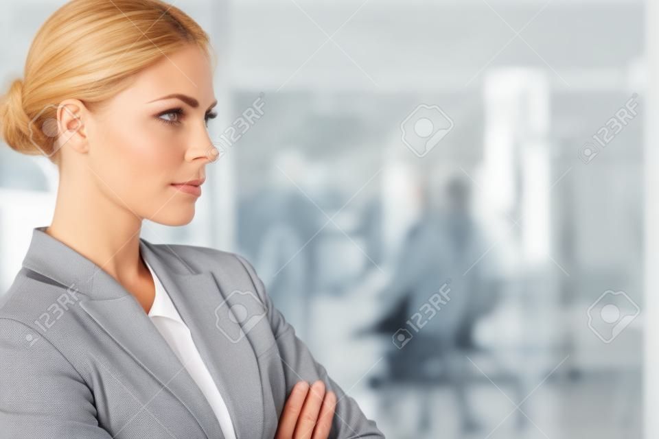 Serious businesswoman standing with arms crossed in a bright office