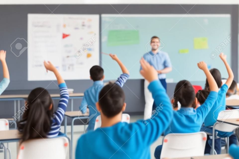 Vista posteriore di studenti con le mani alzate con un insegnante in classe