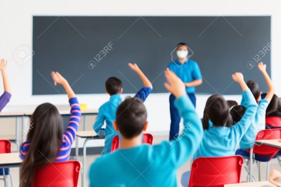 Vista posteriore di studenti con le mani alzate con un insegnante in classe