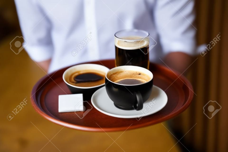 Waiter holding tray with coffee cup and pint of beer in a bar