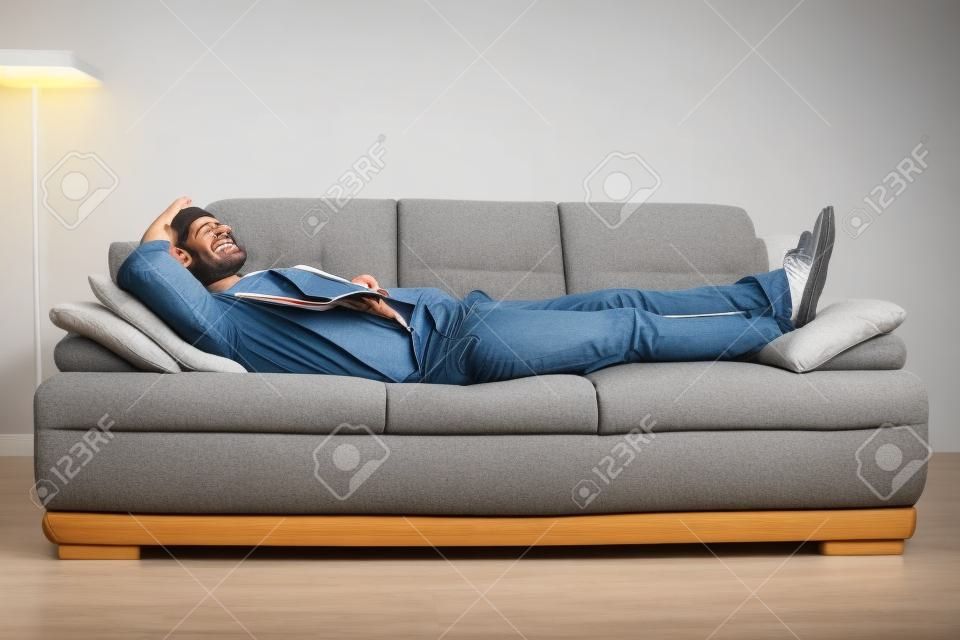 Улыбаясь человек лежал и расслабляющий на диване у себя дома в гостиной