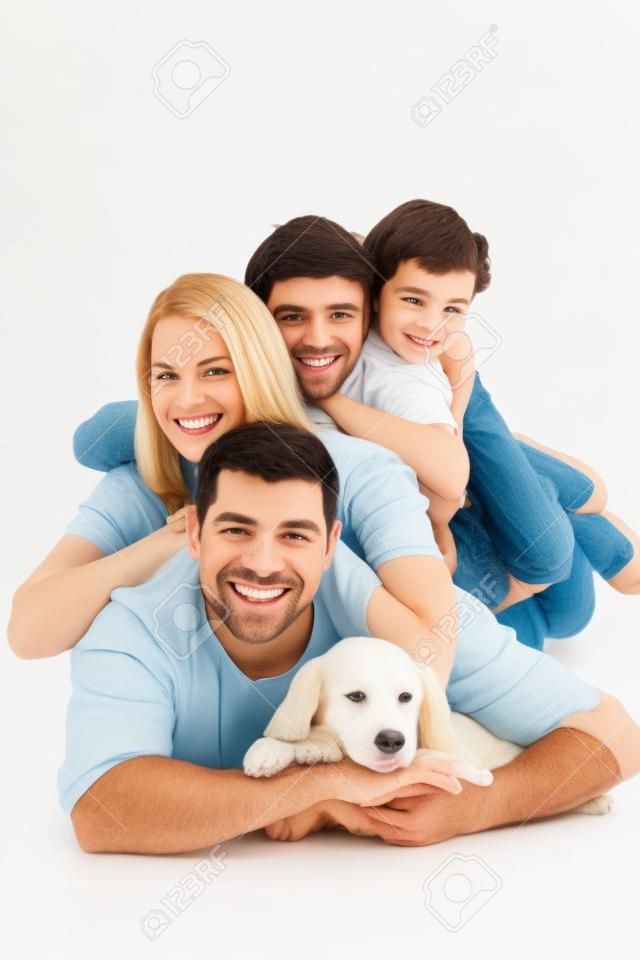 Retrato de familia feliz acostado en uno encima del otro con el perro sobre fondo blanco