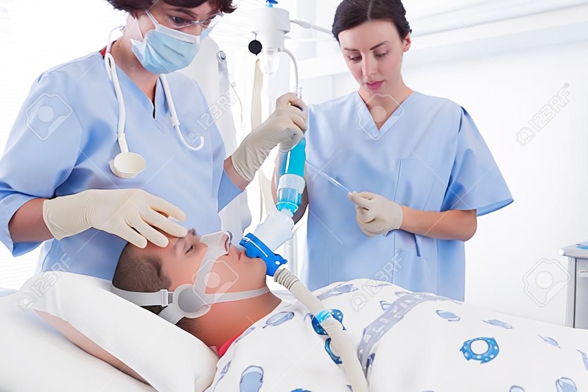 I medici che tengono maschera di ossigeno e l'esame flebo endovenosa nella stanza d'ospedale