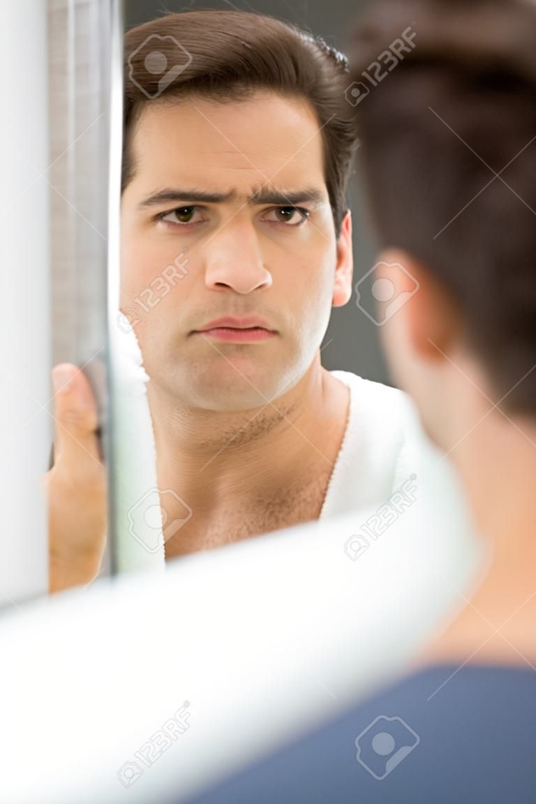 Man looking in mirror and checking his stubble in bathroom