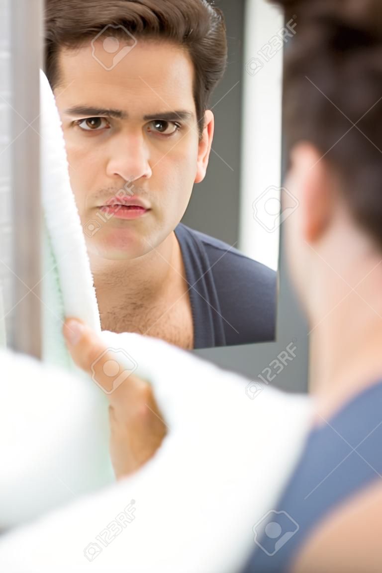 Man looking in mirror and checking his stubble in bathroom