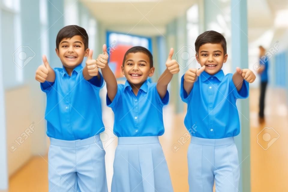 Retrato de la sonrisa de los niños de escuela que muestra los pulgares para arriba en el pasillo en la escuela