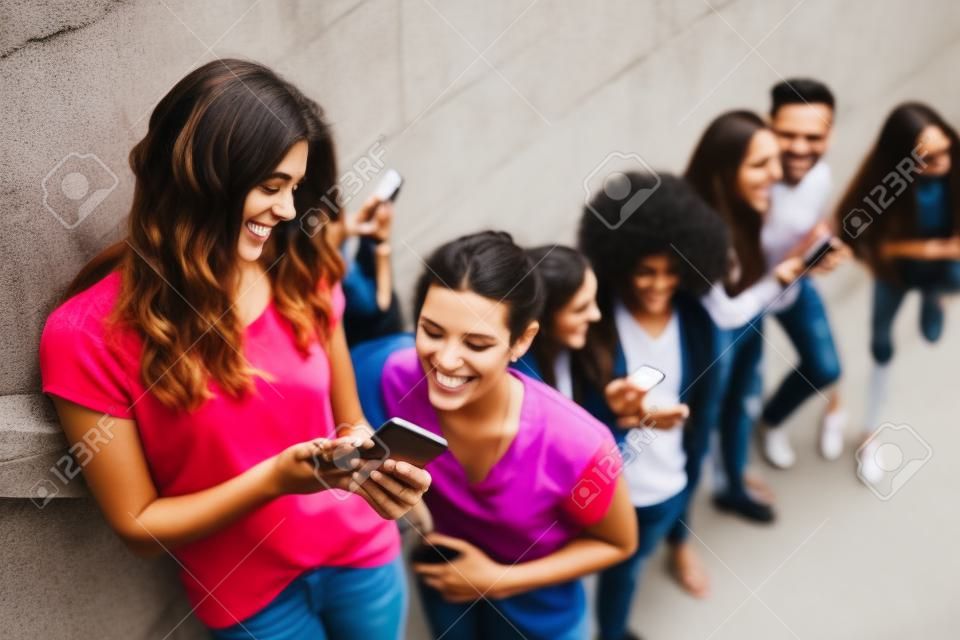 High angle view of happy friends using mobile phones while standing by wall