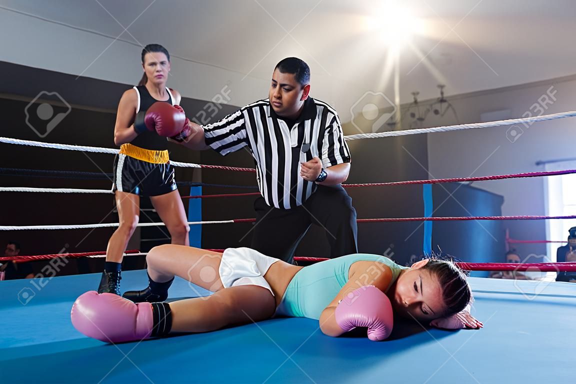 Weiblicher schauender Boxer während der Referent, der vom Athleten im Boxring zählt