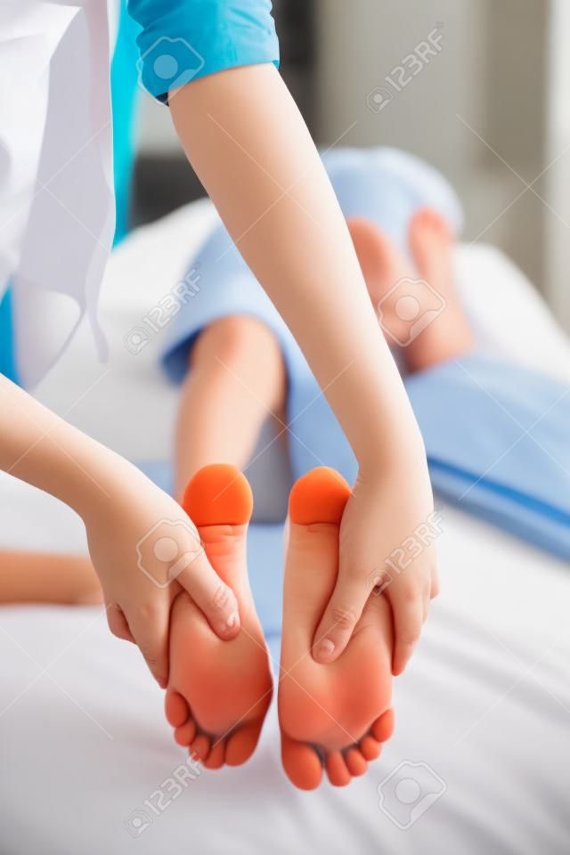 Jongen liggen op bed terwijl het ontvangen van voetmassage van jonge vrouwelijke therapeut op ziekenhuisafdeling