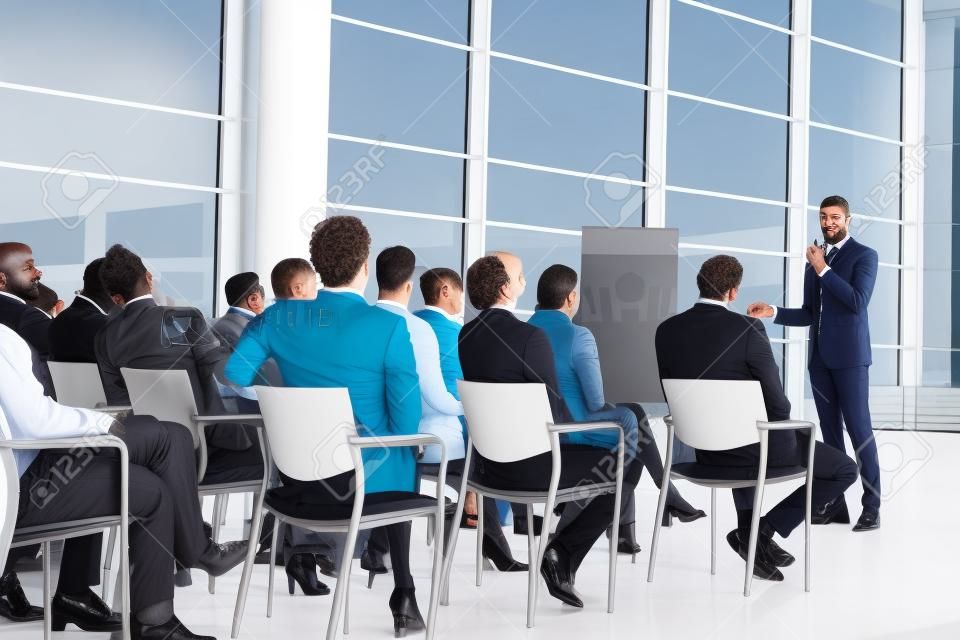 Vue de face d'un bel homme d'affaires métis s'exprimant lors d'un séminaire d'entreprise avec divers hommes d'affaires l'écoutant lors d'une conférence