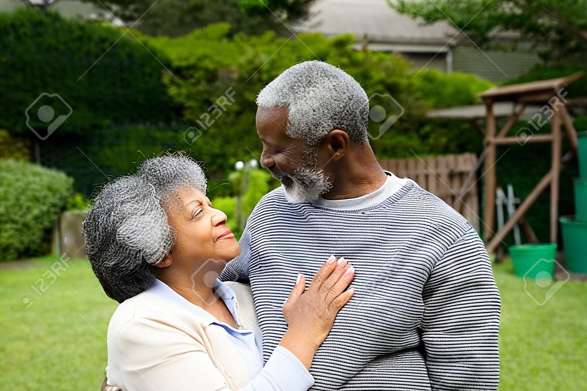 Vista lateral do casal afro-americano sênior no jardim, abraçando-se e olhando um para o outro.