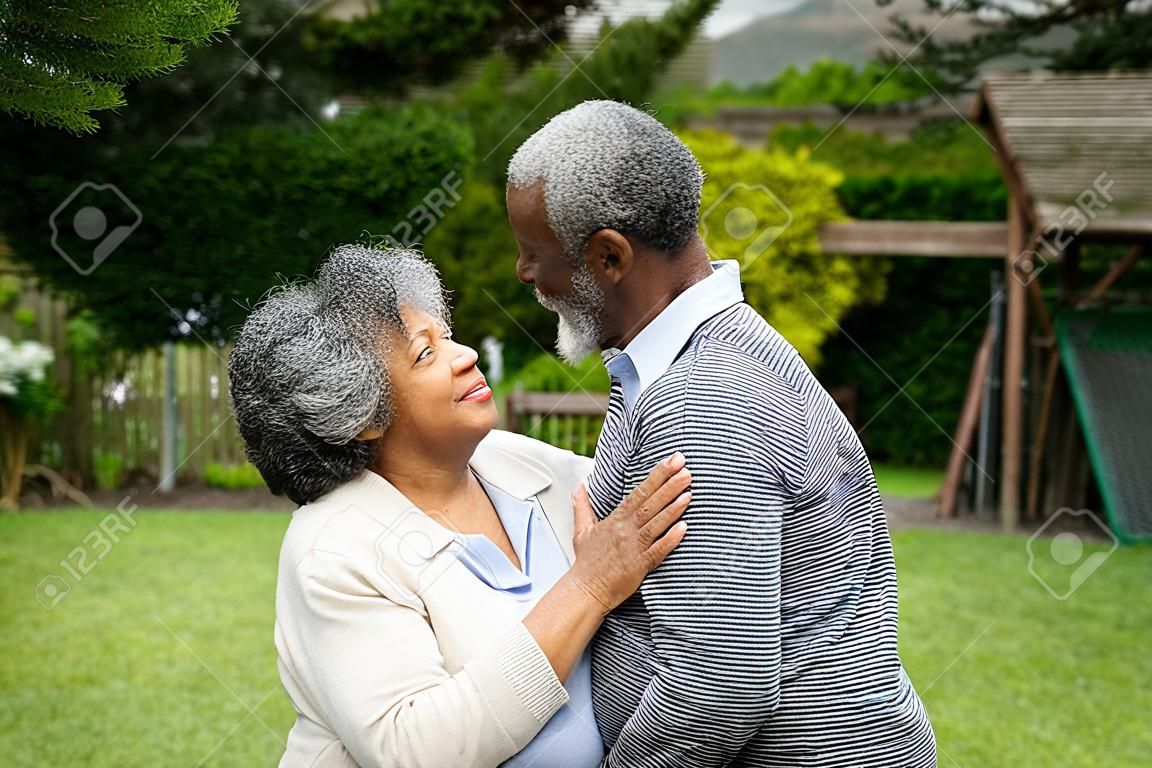 Vista lateral do casal afro-americano sênior no jardim, abraçando-se e olhando um para o outro.
