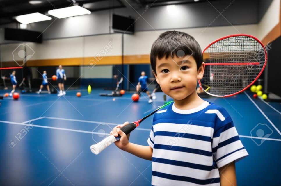 Kleine jongen die badminton racket neemt in de trainingsles in de sportschool