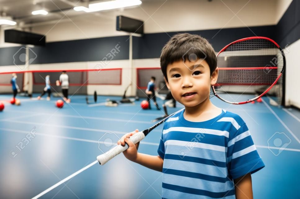 Kleine jongen die badminton racket neemt in de trainingsles in de sportschool