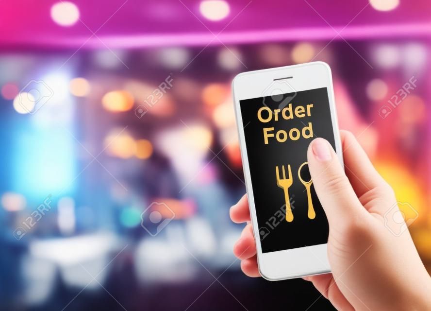 手ぼかしレストランの背景、注文食品 onine ビジネス コンセプトと食べ物を注文で携帯電話を保持しています。
