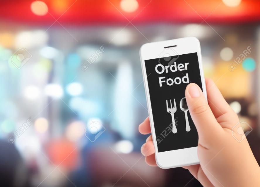 手ぼかしレストランの背景、注文食品 onine ビジネス コンセプトと食べ物を注文で携帯電話を保持しています。