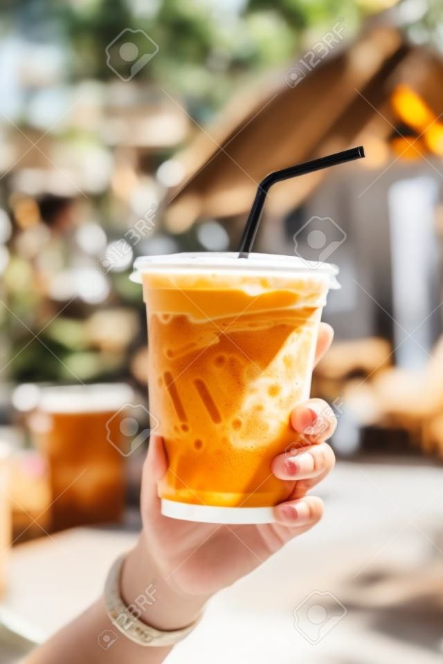 Hand Holding Iced Latte with Straw in Plastic Cup at Garden Blur