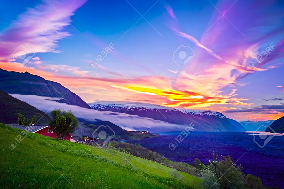 Kleines Dorf mit einer schönen Kulisse an den Flam Fjords, Norwegen. Berge und Fjord in Norwegen. Wolken und blauer Himmel. Schöne atemberaubende Aussicht auf Berge, Wasser, Himmel, Wolken und Sonne. Norwegische Natur