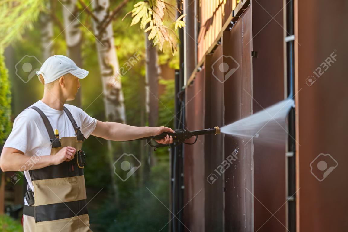 Garage Gate Water Cleaning. Garage Walls and Gate Powerful high Pressure Water Washing. Caucasian Worker Cleaning Building Elements.