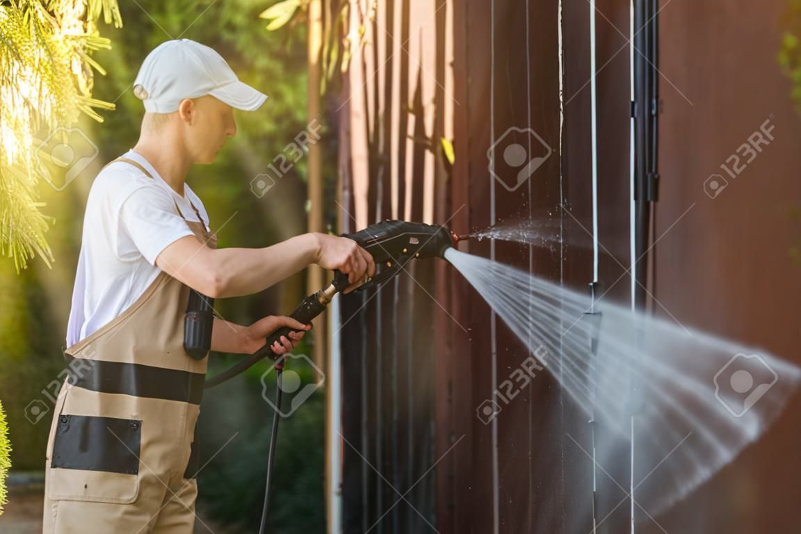 Garage Gate Water Cleaning. Garage Walls and Gate Powerful high Pressure Water Washing. Caucasian Worker Cleaning Building Elements.