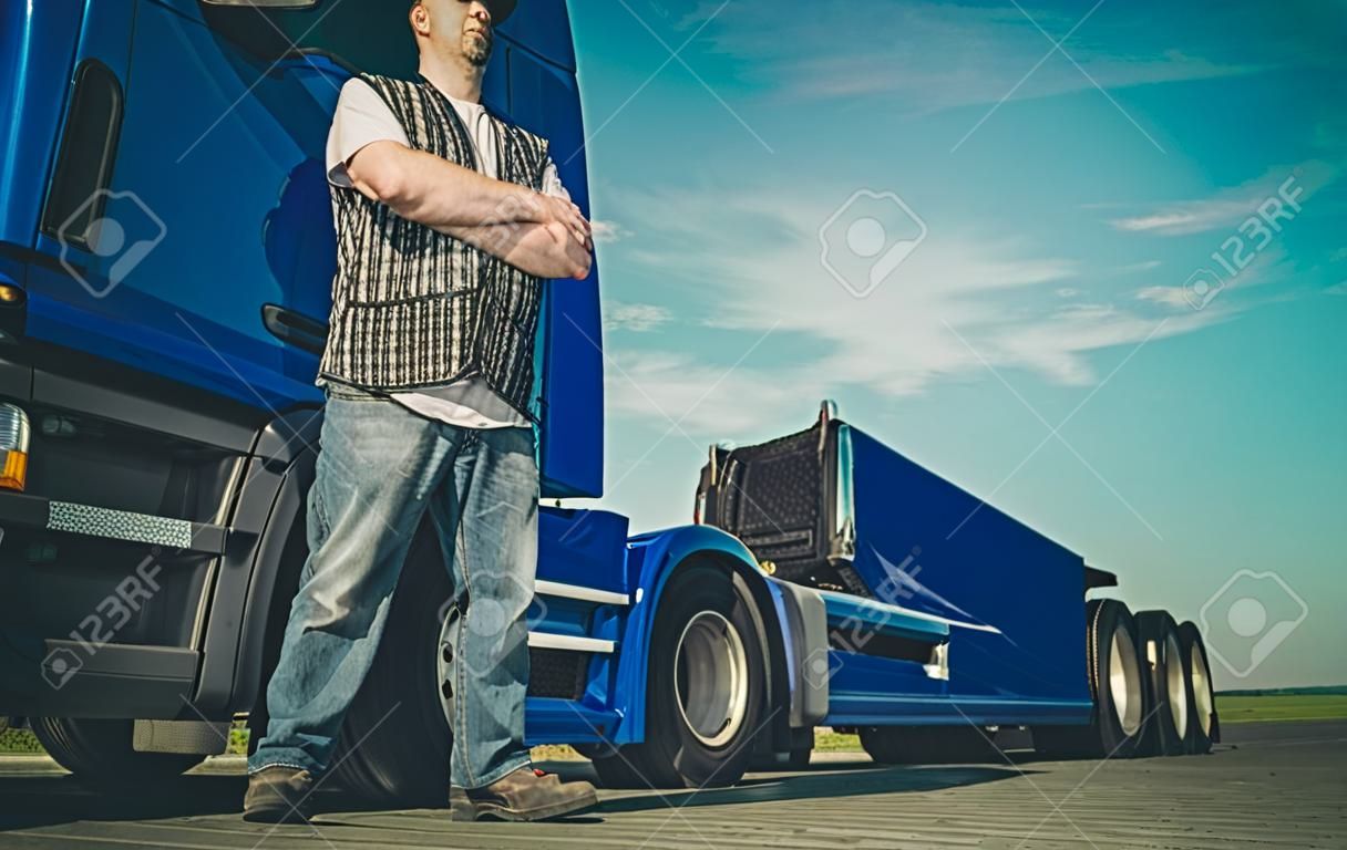 Semi Truck and the Driver. Proud Caucasian Trucker with Crossed Hands. Automotive Industry.