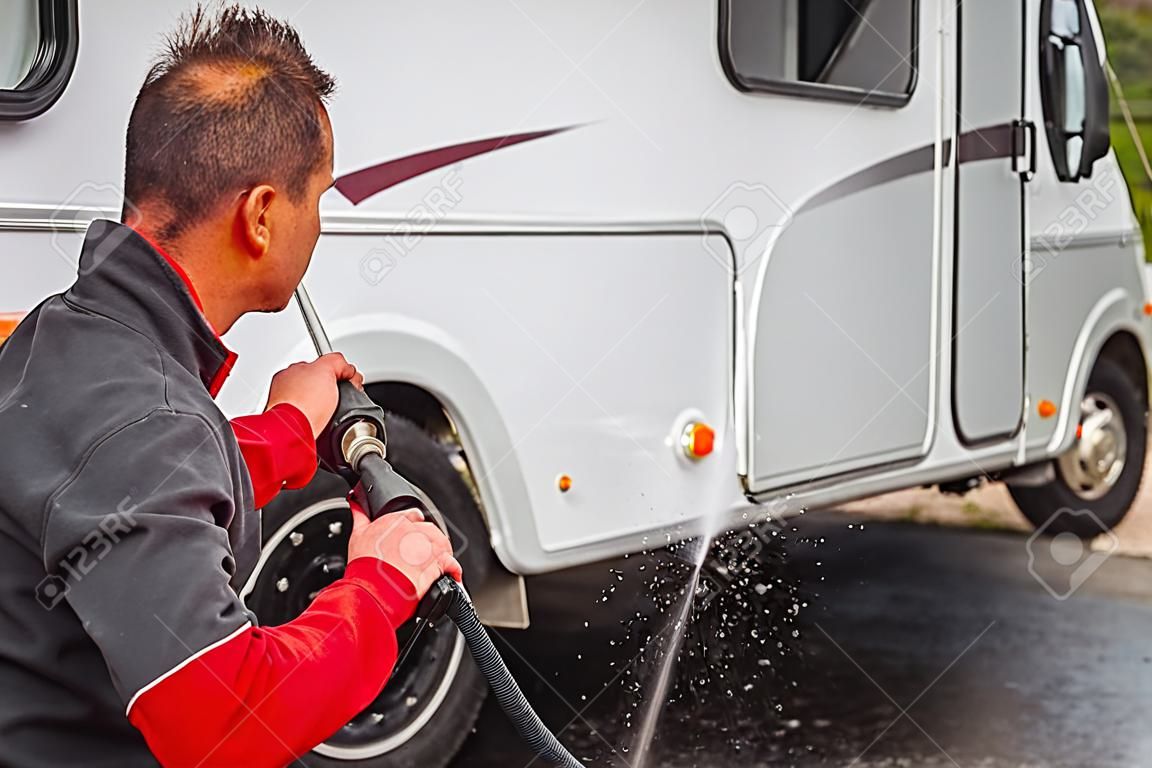 Kaukaski mężczyzna po trzydziestce czyści zewnątrz swojego samochodu kempingowego za pomocą myjki ciśnieniowej.