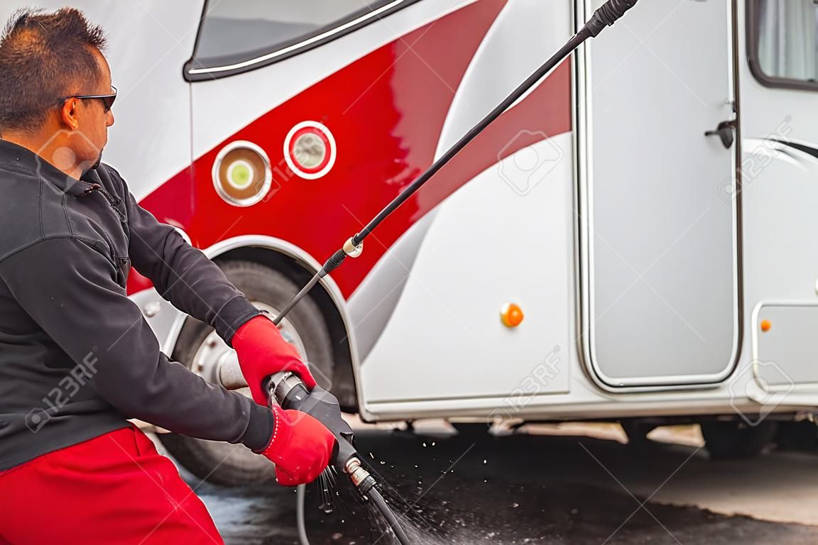 Kaukaski mężczyzna po trzydziestce czyści zewnątrz swojego samochodu kempingowego za pomocą myjki ciśnieniowej.