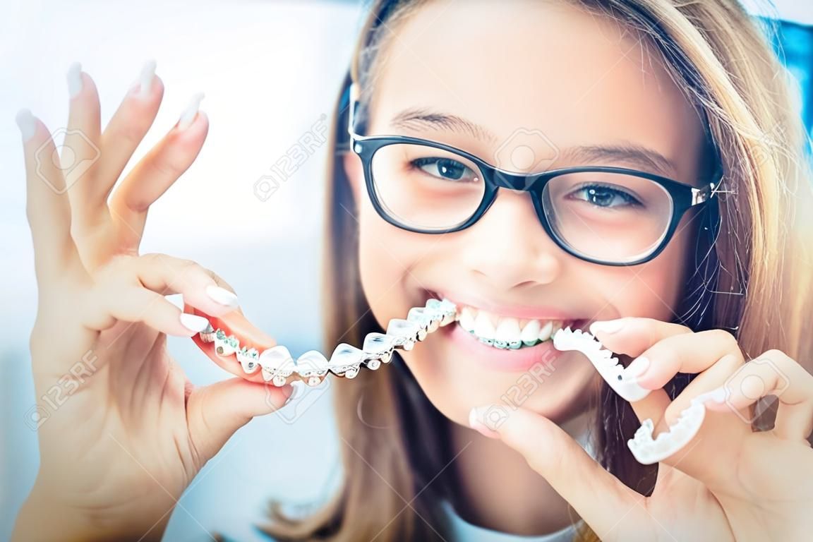 若い笑顔の女の子の手に歯科目に見えないブレースやシリコーンのトレーナー。矯正概念 - インビスアライン。