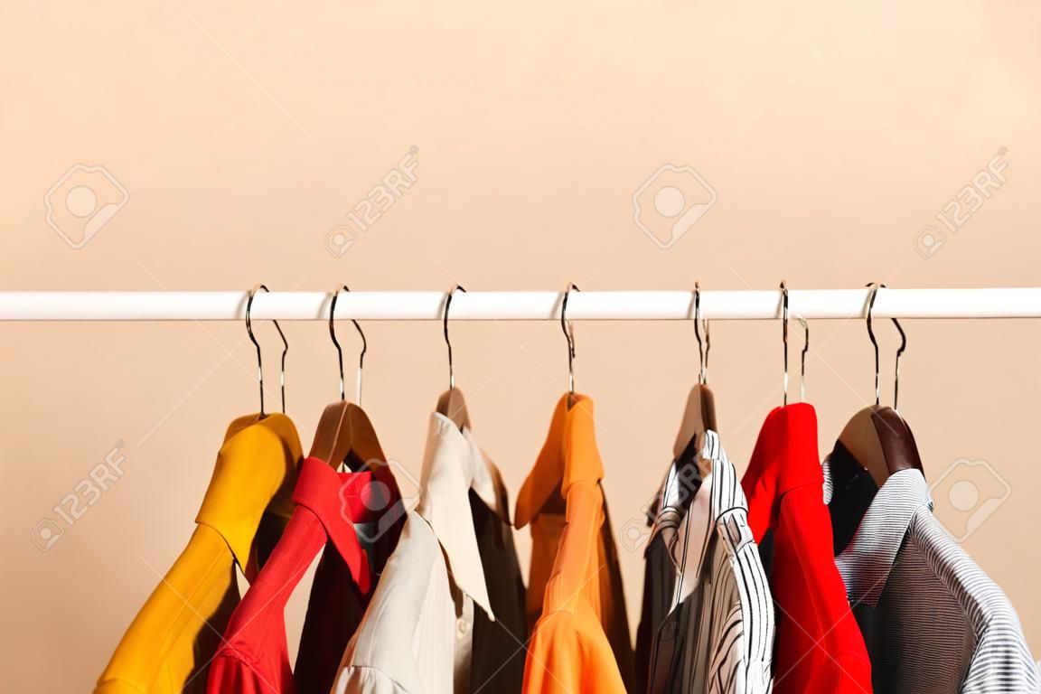 컬러 배경의 옷장 선반에 있는 옷걸이에 있는 세련된 옷.