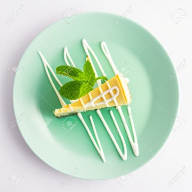 pedaço de cheesecake de baunilha com pétala de hortelã em uma placa circular branca isolada no fundo branco.