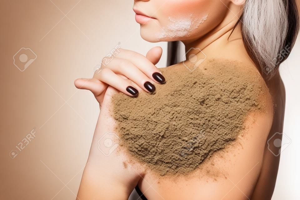 beauty, people and healthy skin concept - Brunette woman cleans skin of the body coffee scrub white background isolated. Beauty Portrait. Beautiful Spa Woman Touching her Face. Perfect Fresh Skin.