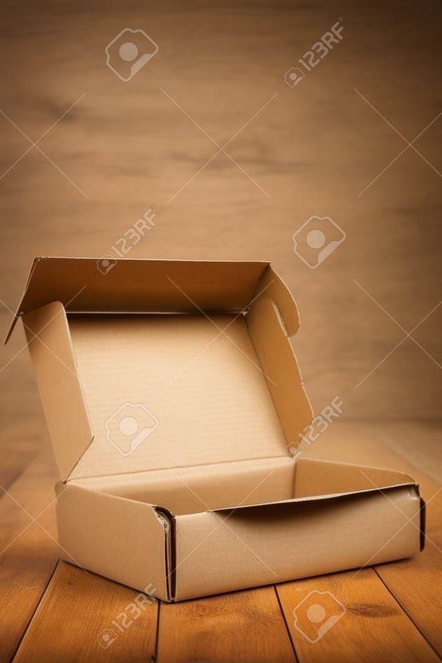 Boîte en carton avec rabat ouvert sur plancher et mur en bois
