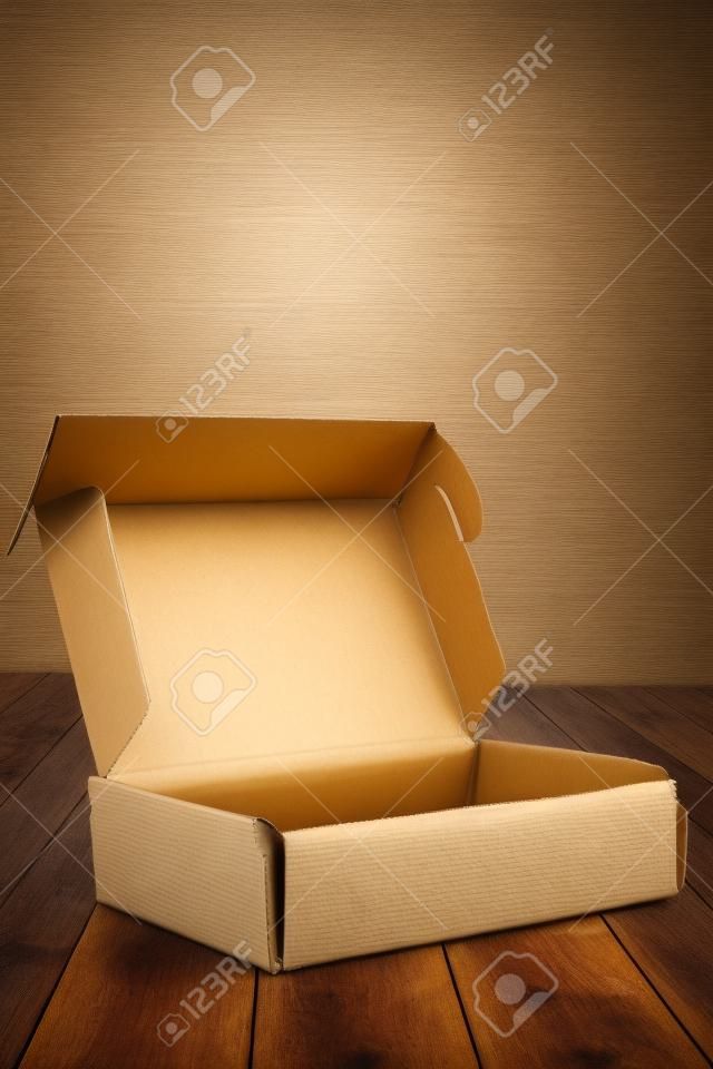 Cardboard box with flip open on wooden floor and wall