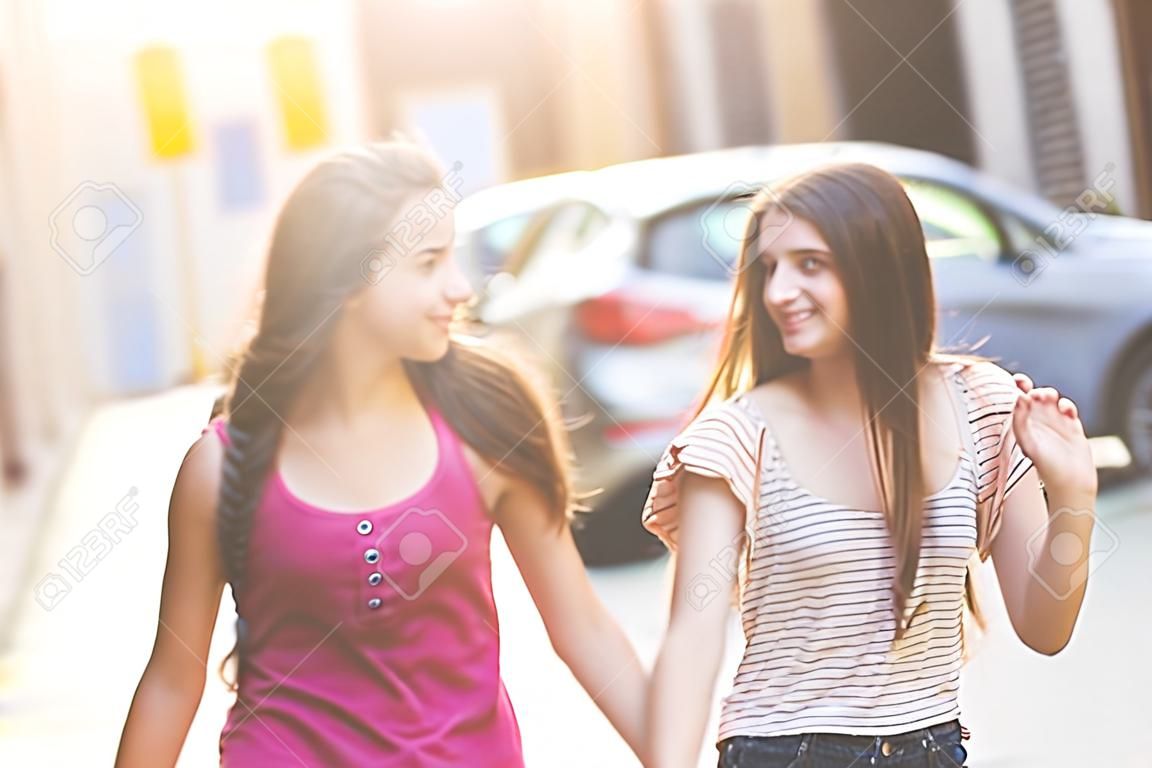 Two girls walking on the street. They are two young girls walking together and  holding their hands. They are wearing summer clothes and they are happy.