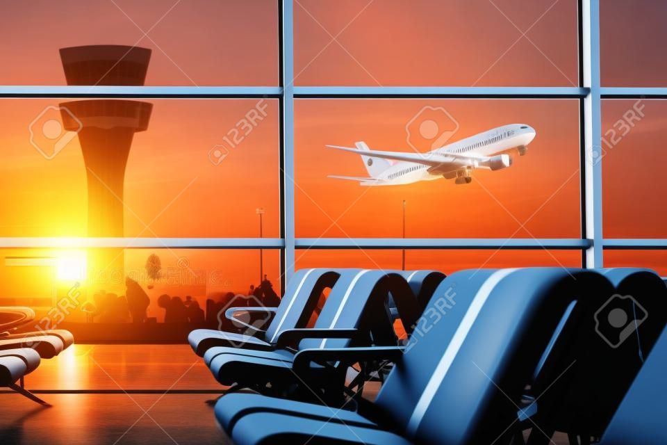 Leere Stühle in der Abflughalle am Flughafen, mit dem Kontrollturm und ein Flugzeug bei Sonnenuntergang auszuziehen. Reise- und Transportkonzepte.