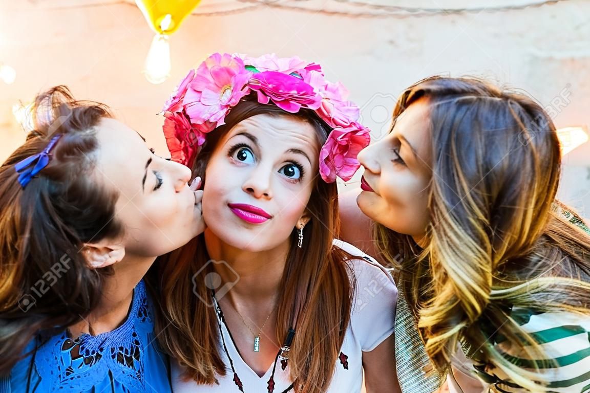 Women kissing a happy girl on her birthday. Three girls having fun during a party at sunset on a rooftop in Barcelona. Friendship and lifestyle concepts.