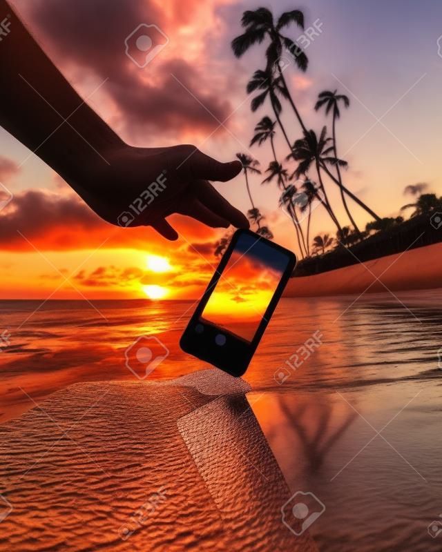 Uma foto de perto de uma pessoa tirando uma foto de palmeiras durante o pôr do sol com um smartphone - legal para fundos