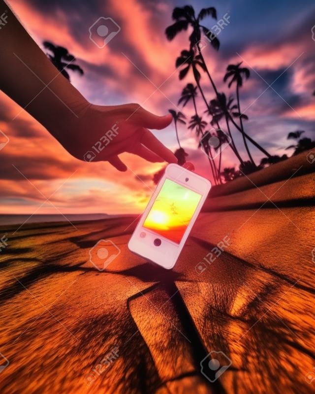 Eine Nahaufnahme einer Person, die während des Sonnenuntergangs mit einem Smartphone ein Foto von Palmen macht - cool für Hintergründe